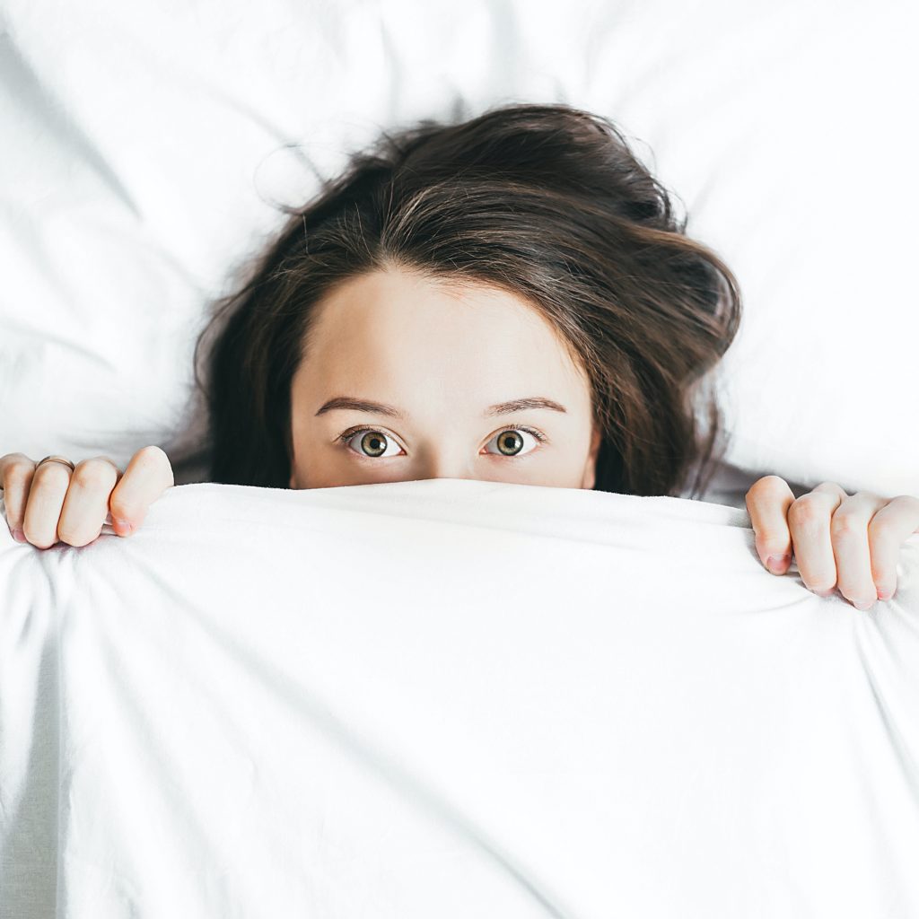 woman covering her face with blanket, fearful of blackheads and comedones